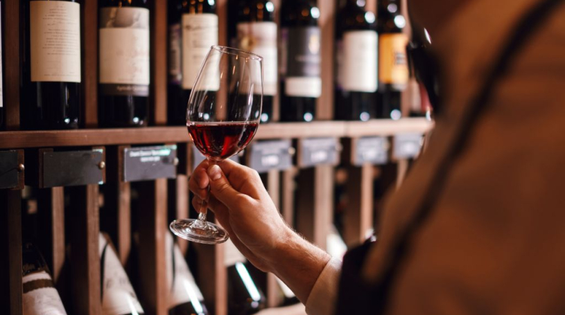 Person holding a glass of wine in front of a bunch of bottles